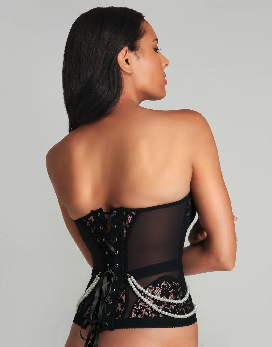 Woman wearing a black lace corset against a gray background