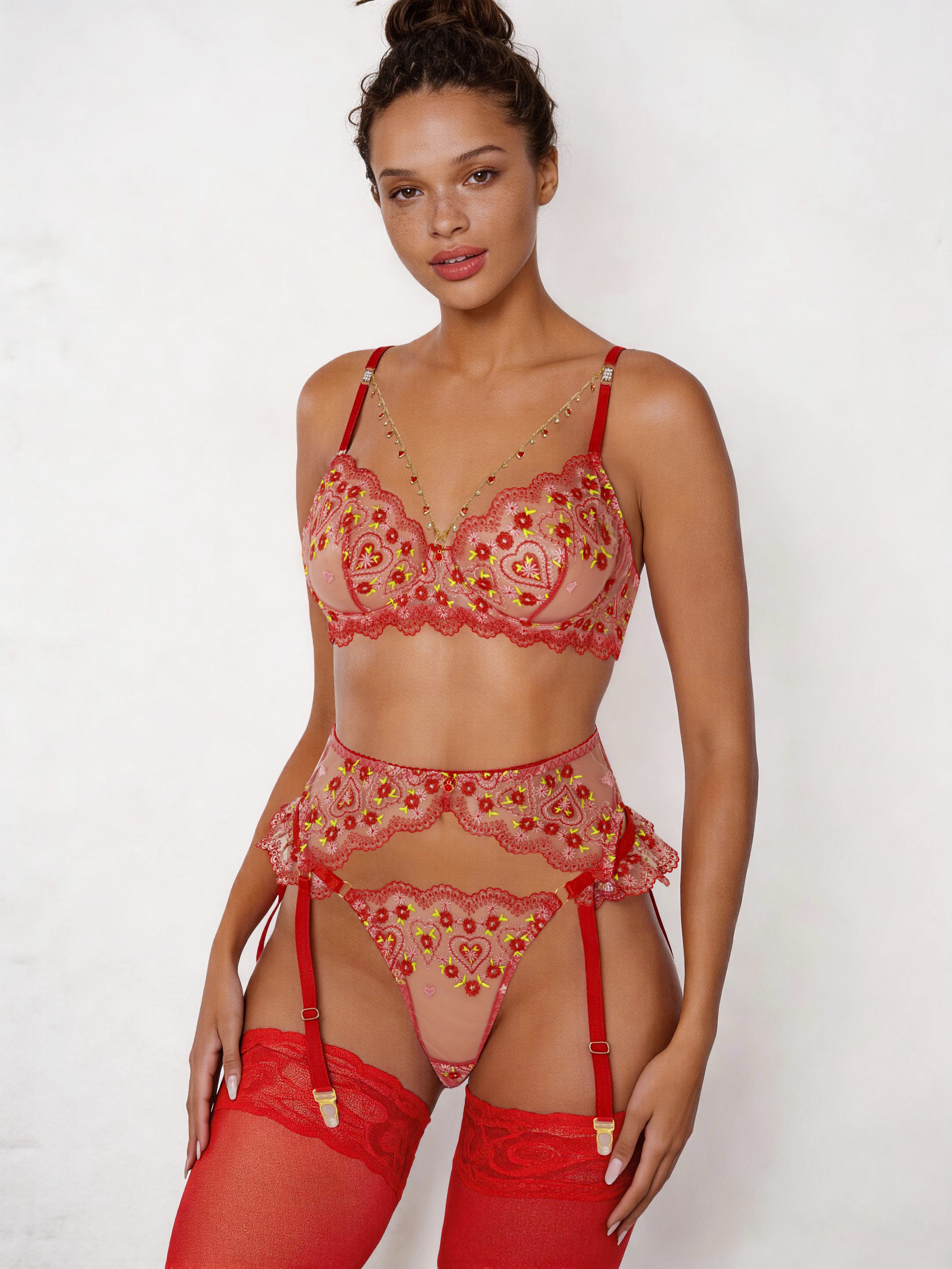 A model wearing a three-piece sheer lace lingerie set in red and pink with gold embroidered details, including a bra, garter belt, thong, and red thigh-high stockings, against a plain white background.