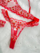 Red lace lingerie set with floral embroidery and heart motifs, laid flat on a white textured background.